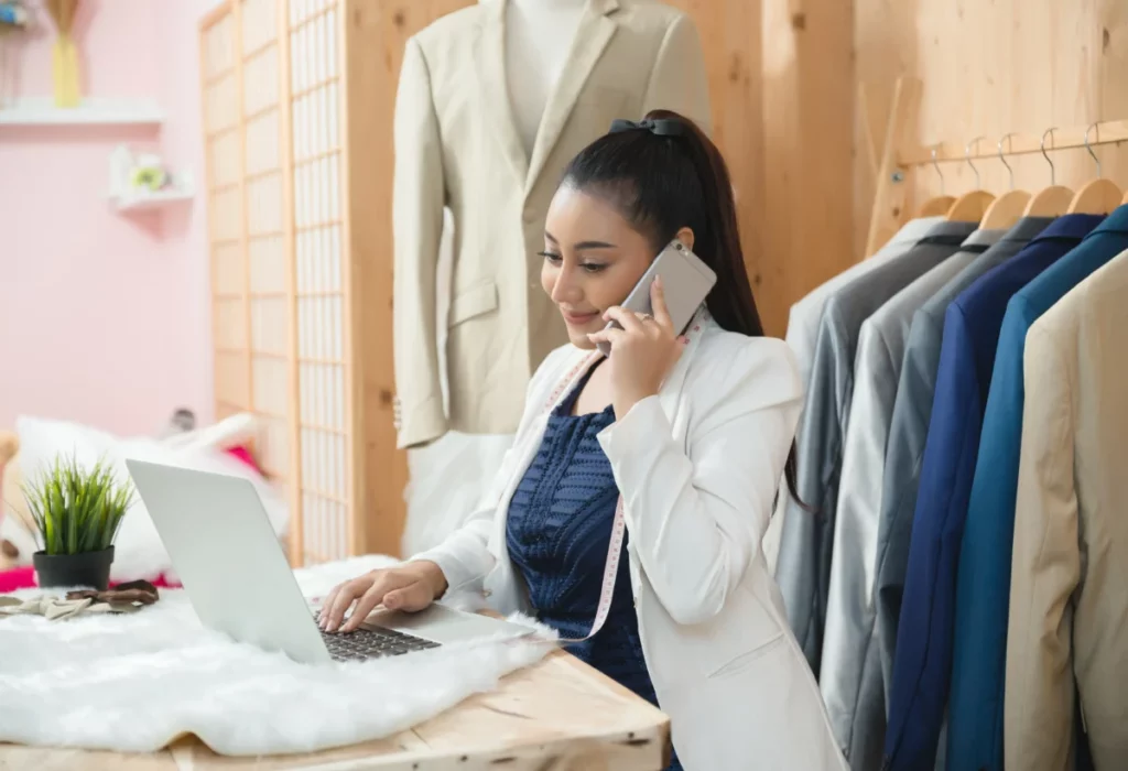 empresária trabalhando em alfaiateria em frente ao computador e falando ao telefone - estratégia de preço