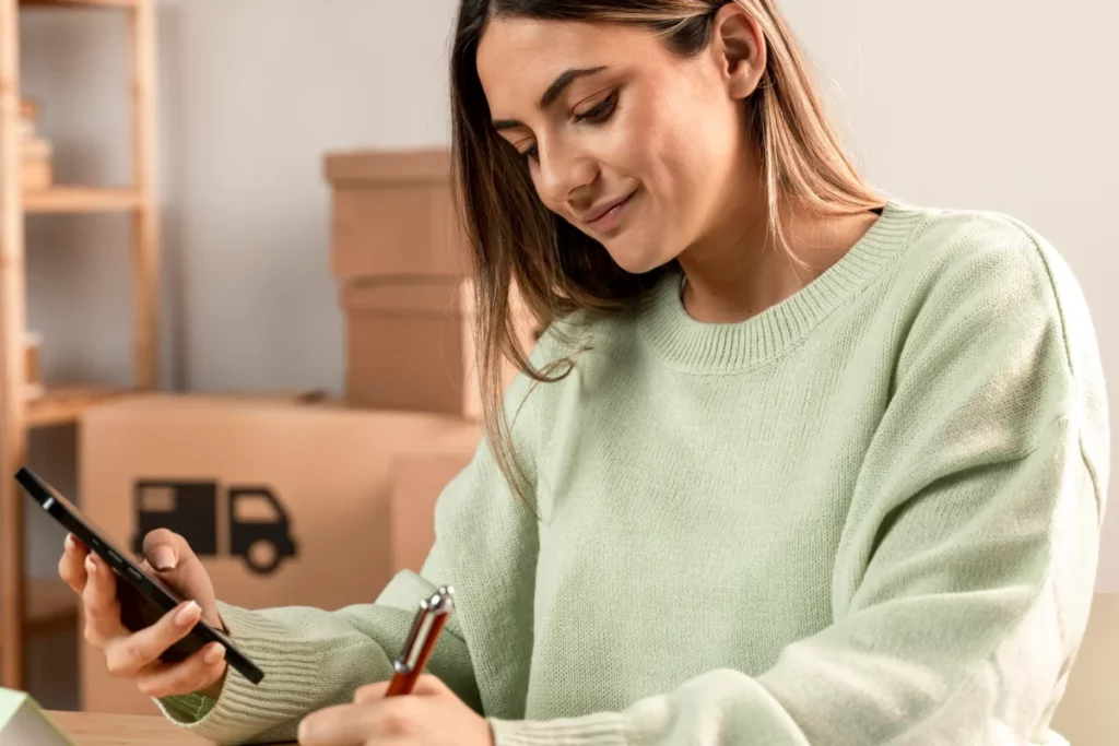 mulher empreendedora escrevendo com uma mão e segurando celular com outra - comprar no atacado para revender