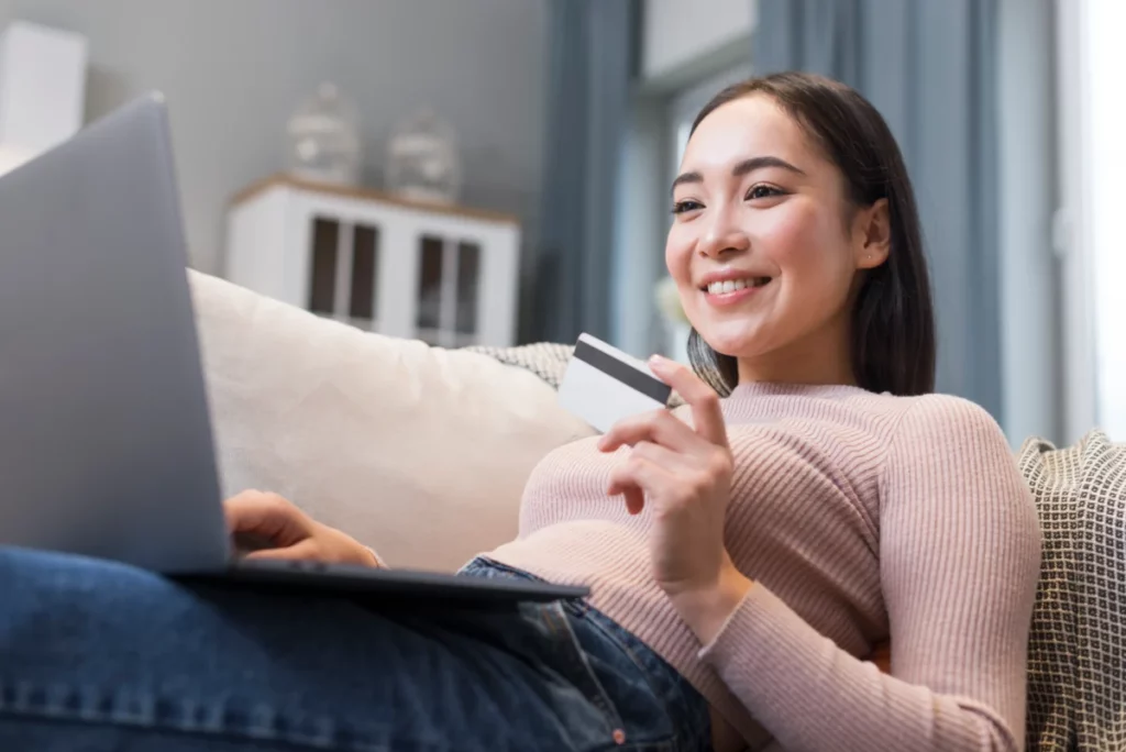 mulher segurando cartão e deitada em sofá com notebook no colo - como criar cupom de desconto