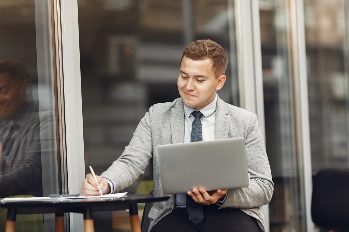 homem de negócios sentado ao ar livre mexendo no computador e anotando em papel - curso de marketplace