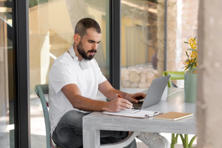 homem sentado em casa mexendo no computador e escrevendo em papel - amazon marketplace