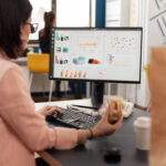 Empreendedora analisando dashboard de e-commerce em computador com gráficos de vendas e pedidos