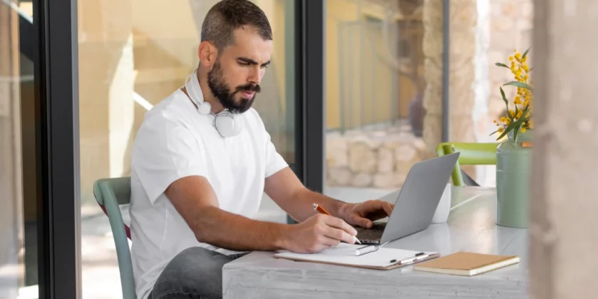 homem sentado em casa mexendo no computador e escrevendo em papel - amazon marketplace